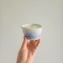 Load image into Gallery viewer, A hand holds a handmade ceramic massage candle in a dark blue to light blue speckle pattern against a white background.