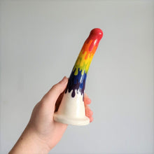 Load image into Gallery viewer, A hand holds a 7 inch curved ceramic dildo in a rainbow drip pattern in front of a white background.