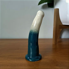 Load image into Gallery viewer, A 6 inch curved ceramic dildo in a white and dark green gradient pattern stands on a wooden table against a white background.