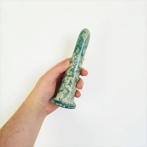 A hand holds a 6 inch classic dildo in a dark green bubble pattern in front of a white background.