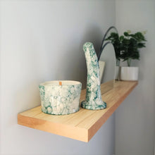 Load image into Gallery viewer, A handmade ceramic massage candle and a 6 inch curved ceramic dildo in a dark green bubble pattern stand at the end of a wooden shelf on a light grey wall. Two circular mirrors are inset into the shelf in the background, and a green plant in a white pot is visible at the other end of the shelf.
