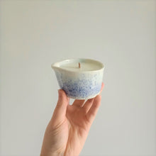 Load image into Gallery viewer, A hand holds a handmade ceramic massage candle in a dark blue to light blue speckle pattern against a white background.
