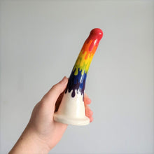 Load image into Gallery viewer, A hand holds a 7 inch curved ceramic dildo in a rainbow drip pattern in front of a white background.
