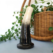 Load image into Gallery viewer, A 5 inch curved ceramic dildo in a white and black gradient pattern stands on a pale blue surface, against a white background. A pot plant flows behind the dildo from a pot in a wicker hanging basket.
