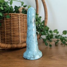 Load image into Gallery viewer, A 5 inch classic ceramic dildo in light blue with a black bubble pattern stands on a wooden surface with a white background. A green plant flows from a wicker basket in the background.
