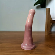 Load image into Gallery viewer, A pink and light purple gradient patterned 5 inch curved ceramic dildo stands on a wooden surface against a white background.
