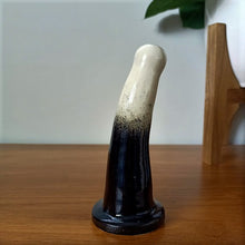 Load image into Gallery viewer, A 5 inch curved ceramic dildo in a white and black gradient pattern stands on a wooden surface, against a white background.
